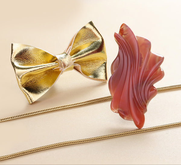 Gold bow tie and red floral hair clip on a beige background